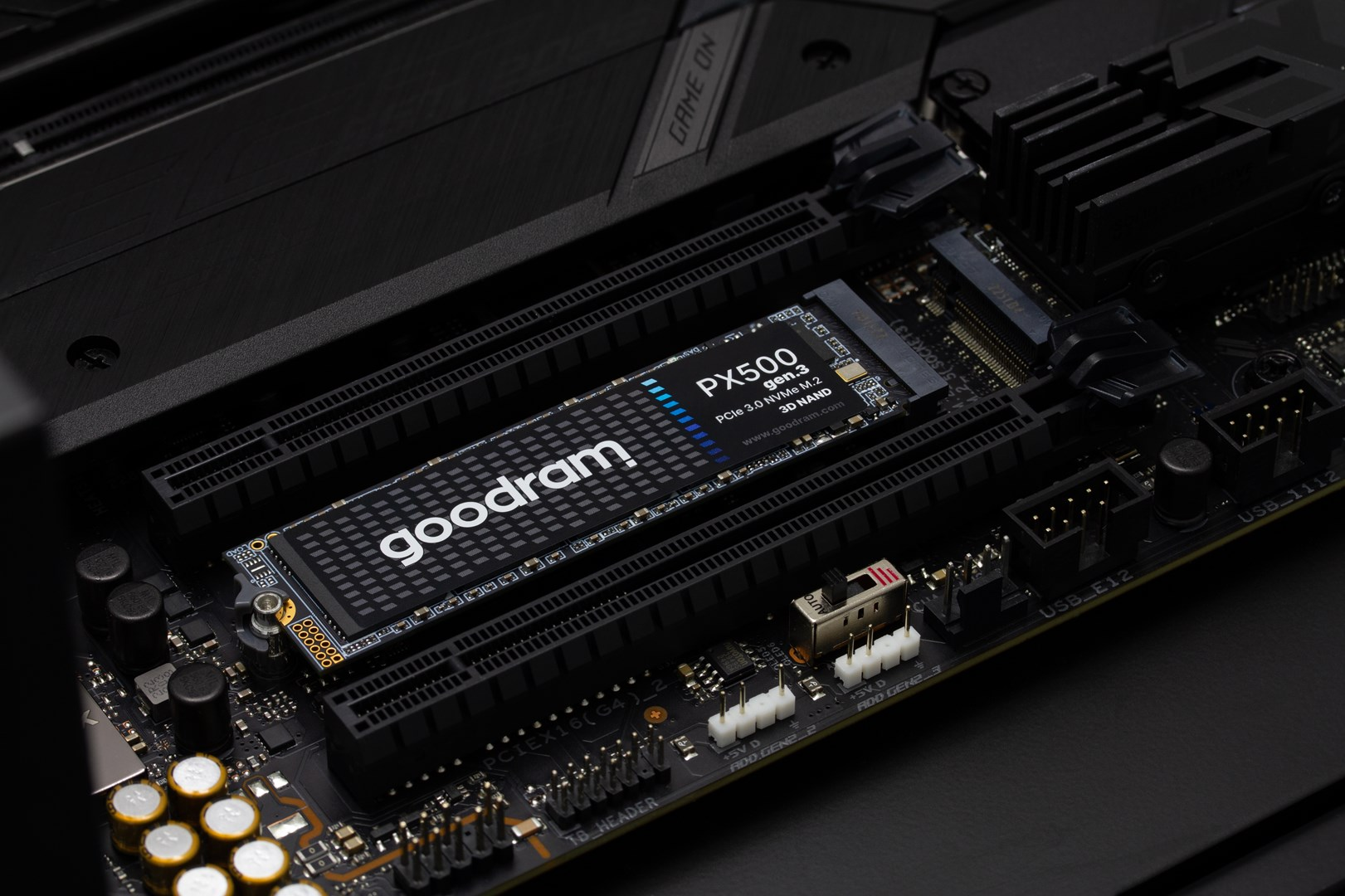 Gros plan sur une carte mère d'ordinateur avec un SSD Goodram PX500 installé. Les tons noirs et gris foncé dominent l'image.