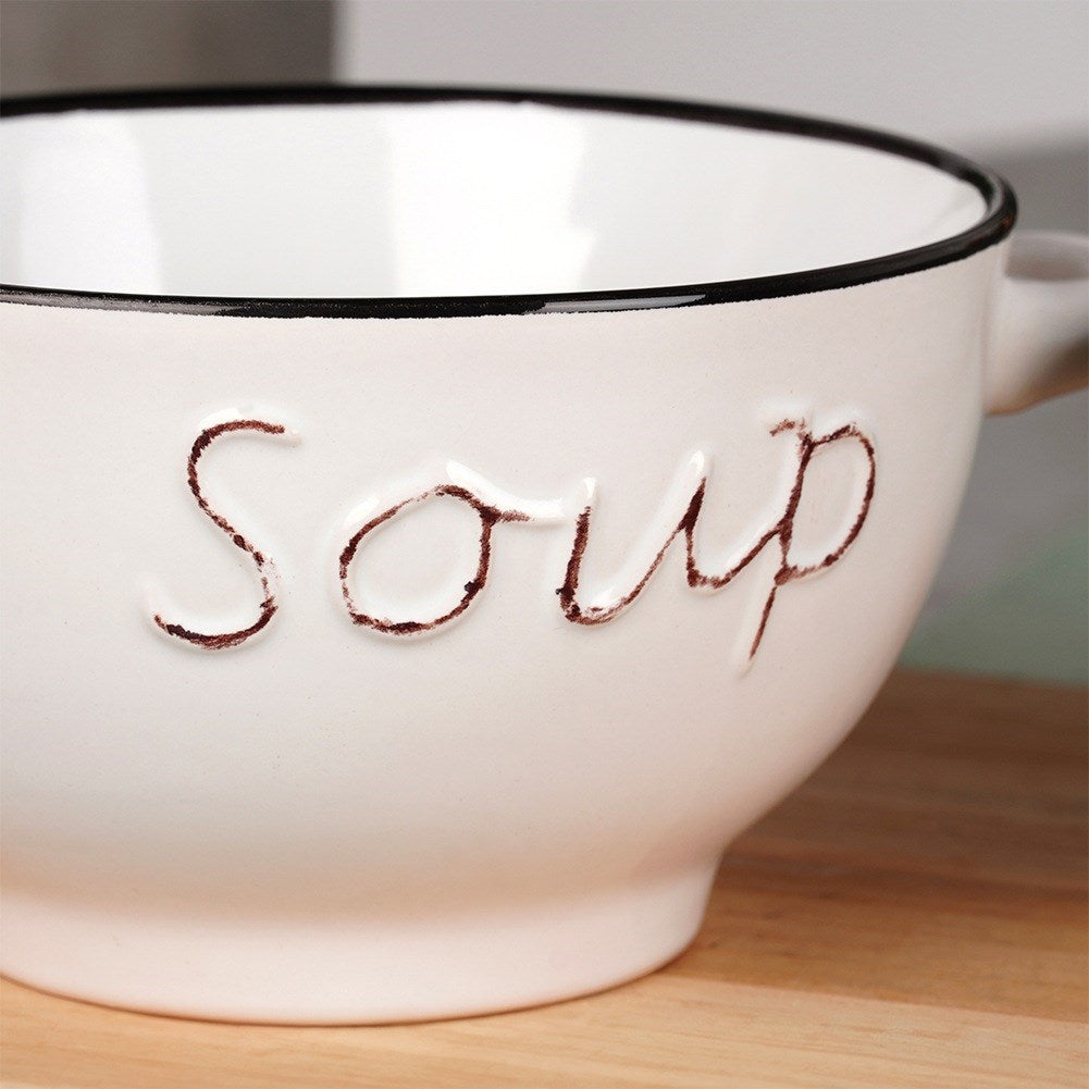 Un cuenco blanco para sopa con borde negro. La palabra 'sopa' está escrita en letras marrones en el lateral. Se encuentra sobre una superficie de madera.