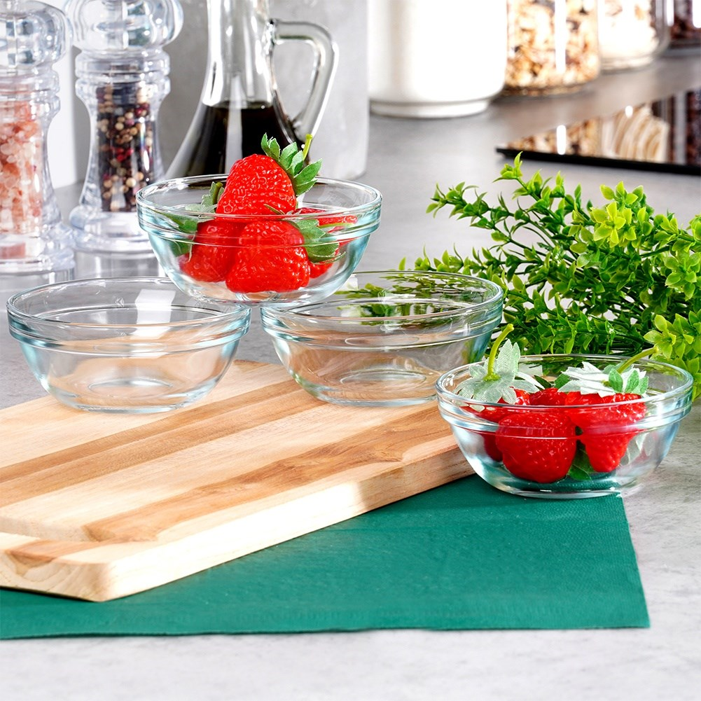 Quattro ciotole di vetro, alcune con fragole, su un tagliere di legno e un tappetino verde. Saliere e pepiere dietro.
