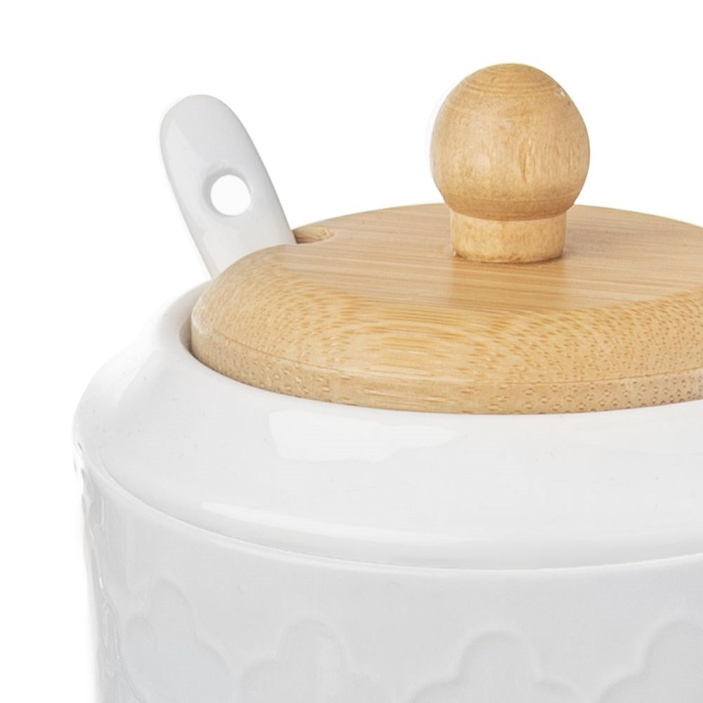 Primo piano di zuccheriera in ceramica bianca con coperchio e pomello in legno. Un cucchiaio bianco è appoggiato sul coperchio.