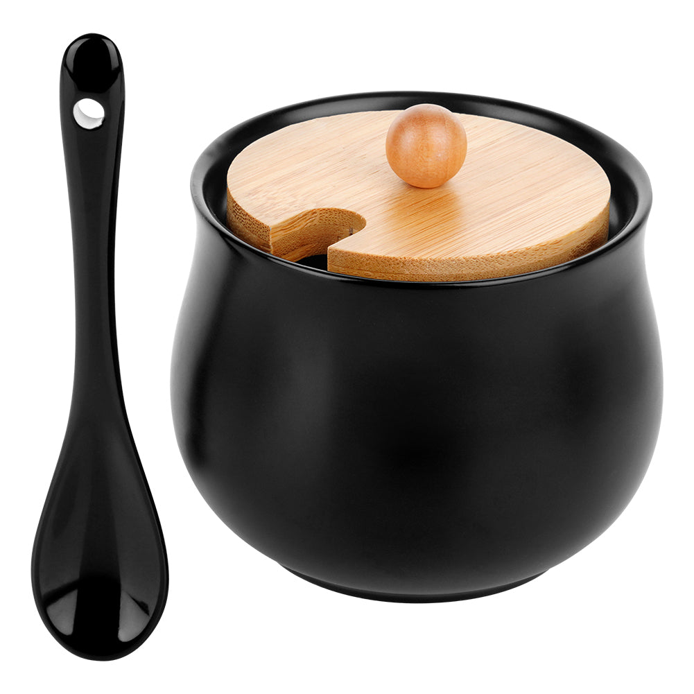 Una zuccheriera in ceramica nera con coperchio in legno e un piccolo pomello in legno, accanto a un cucchiaio nero.