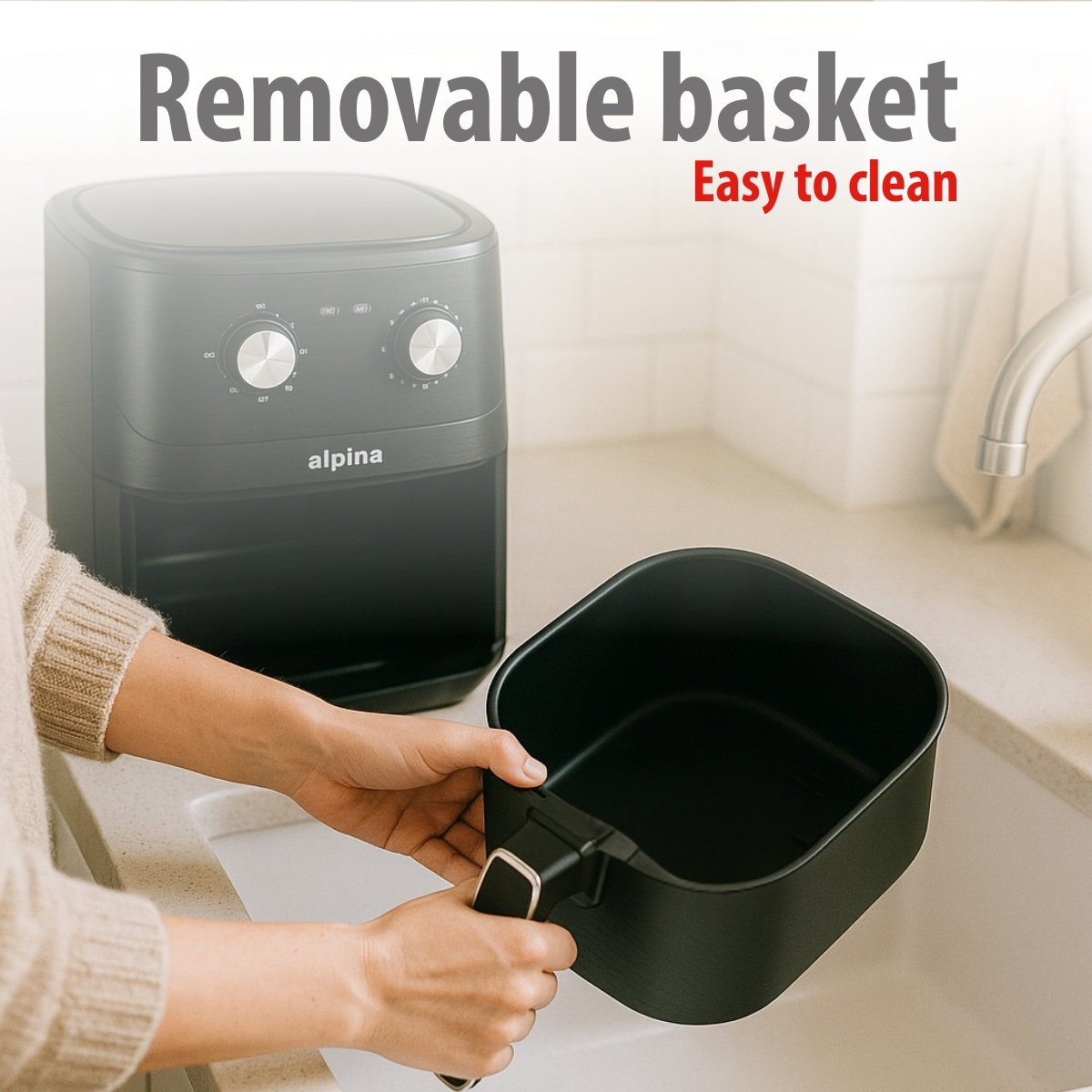 Een persoon houdt een zwarte airfryer-mand vast. Op de achtergrond staat een zwarte airfryer. De tekst luidt 'Uitneembare mand Gemakkelijk schoon te maken'.