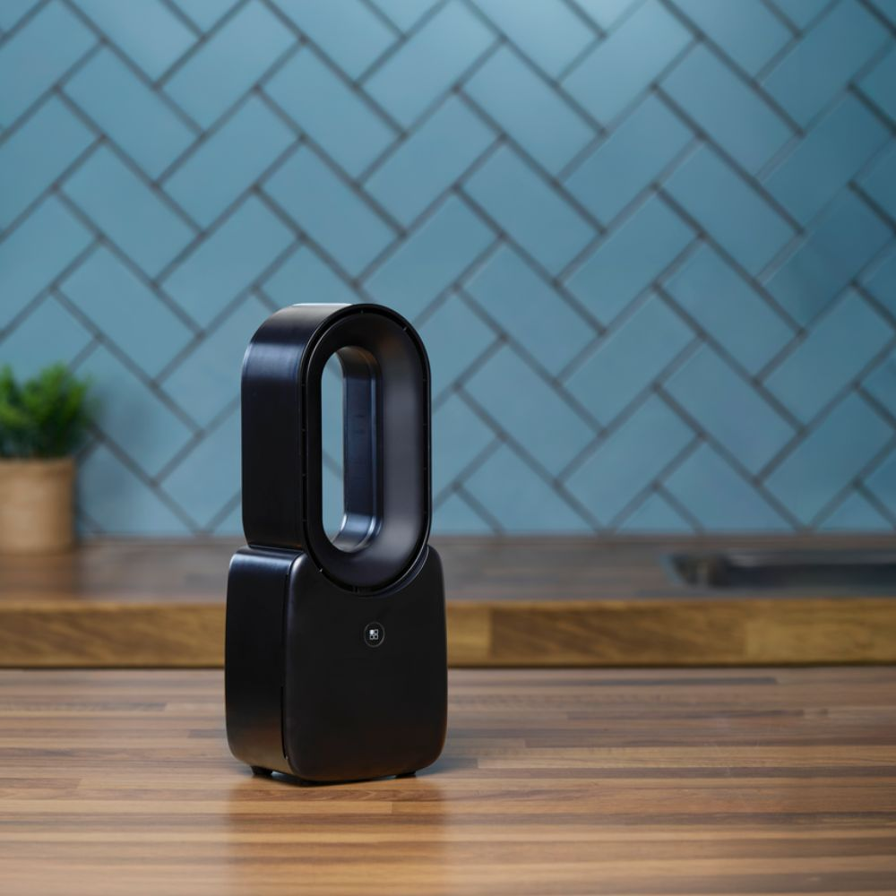 A black air purifier sits on a wood surface. A blue tile backsplash is in the background. A small plant is visible to the left.