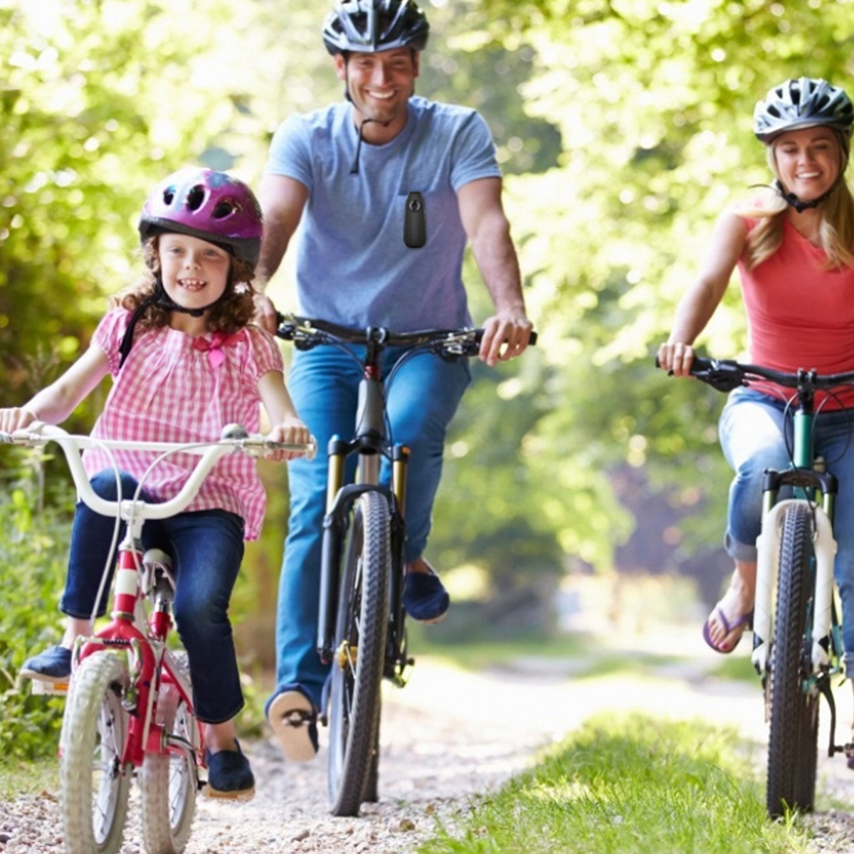 Dreiköpfige Familie fährt auf einem Weg durch Bäume Rad. Vater in Blau, Mutter in Rot und Tochter in Pink, alle lächeln.