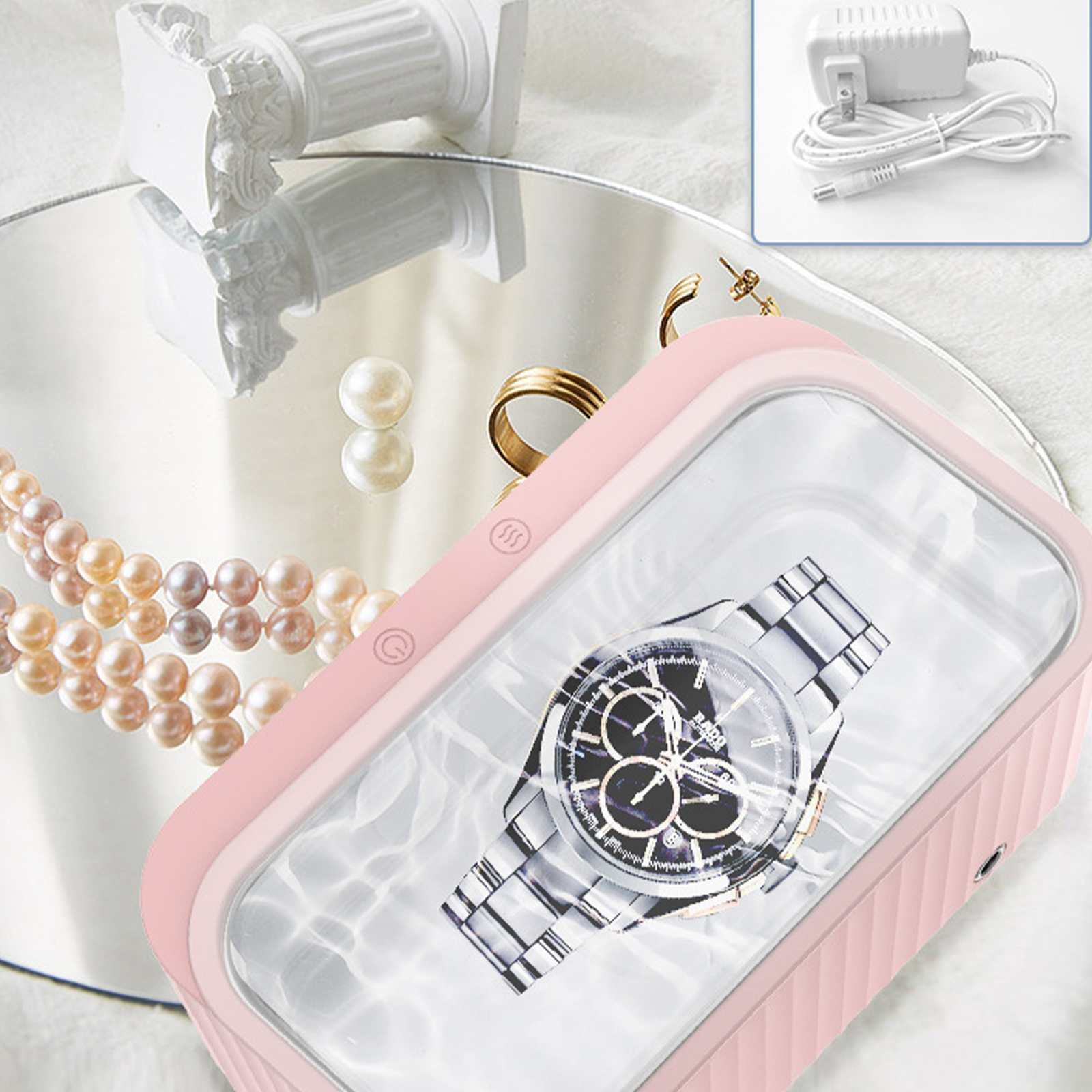 Ein rosa Ultraschallreiniger mit Uhr, Schmuck und Accessoires. Ein kleiner weißer Netzadapter ist oben rechts.