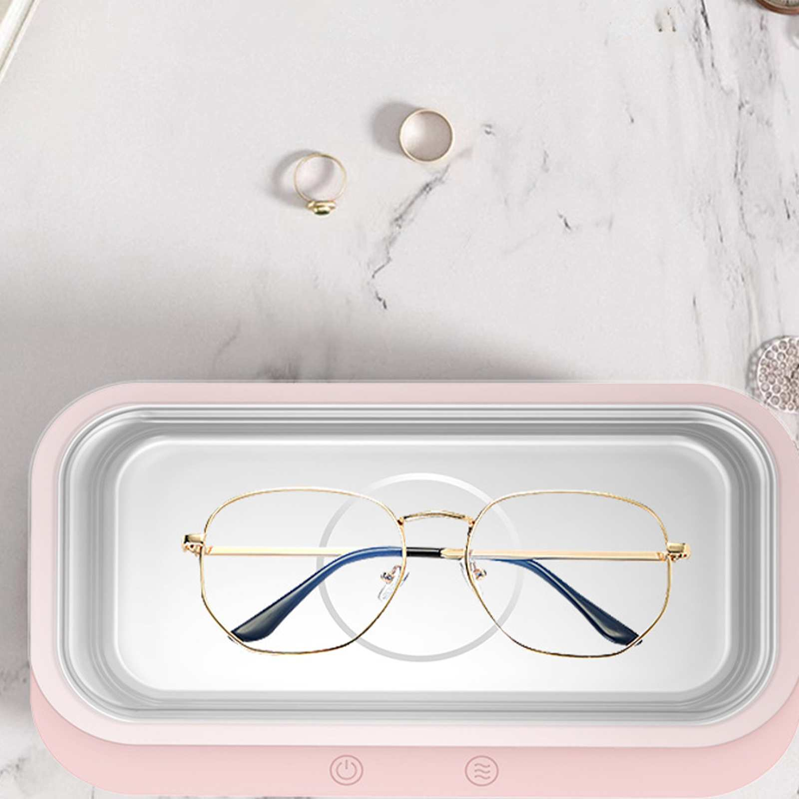 Brille in einem rosa Reinigungsgerät, mit Ringen auf weißer Oberfläche. Die Brille hat einen goldenen Rahmen und blaue Bügel.