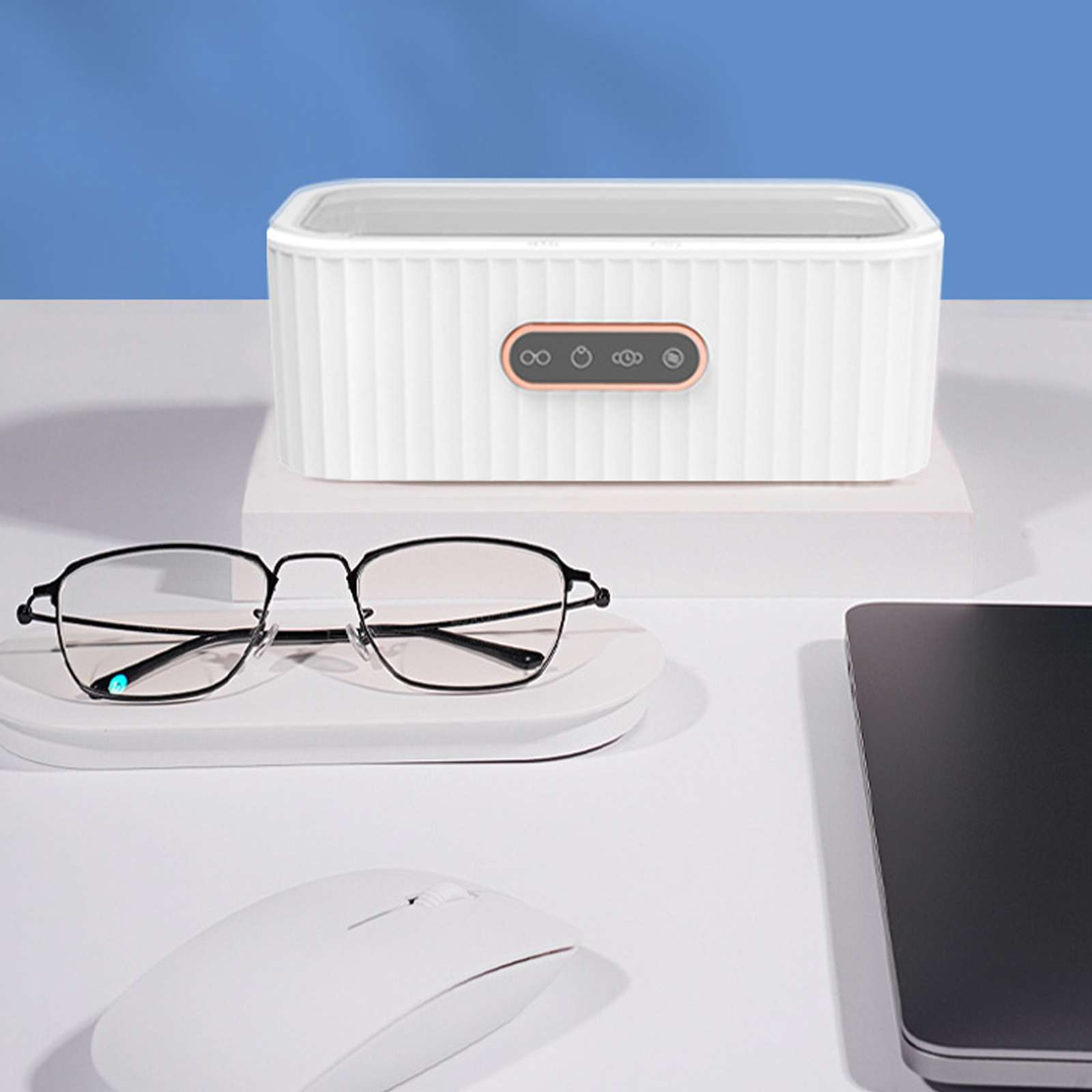 Weißer Brillenreiniger mit Brille und Zubehör auf weißem Schreibtisch, blauer Hintergrund.