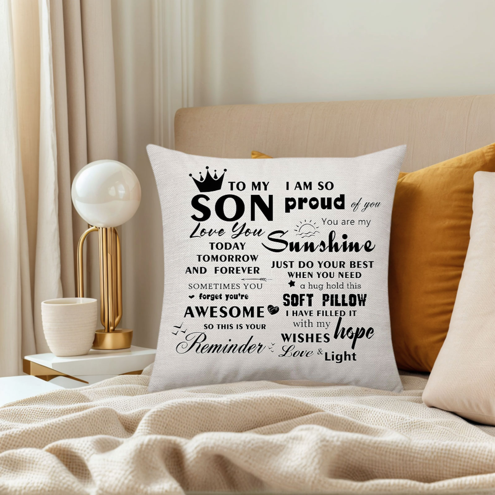 Ein weißes Kissen mit einer Botschaft für einen Sohn auf einem Bett. Es ist von Kissen und einer Lampe umgeben.