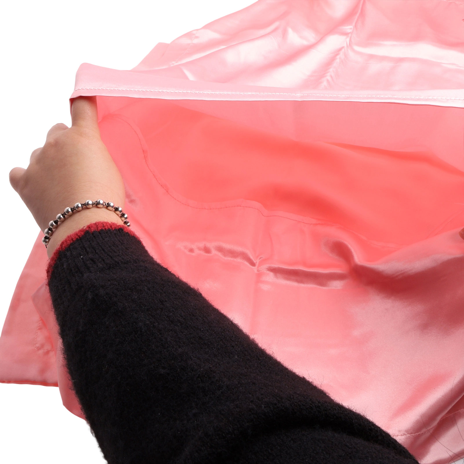 Eine Hand hält einen rosafarbenen Satin-Stoff hoch. Die Person trägt einen schwarzen Pullover und ein silbernes Armband.
