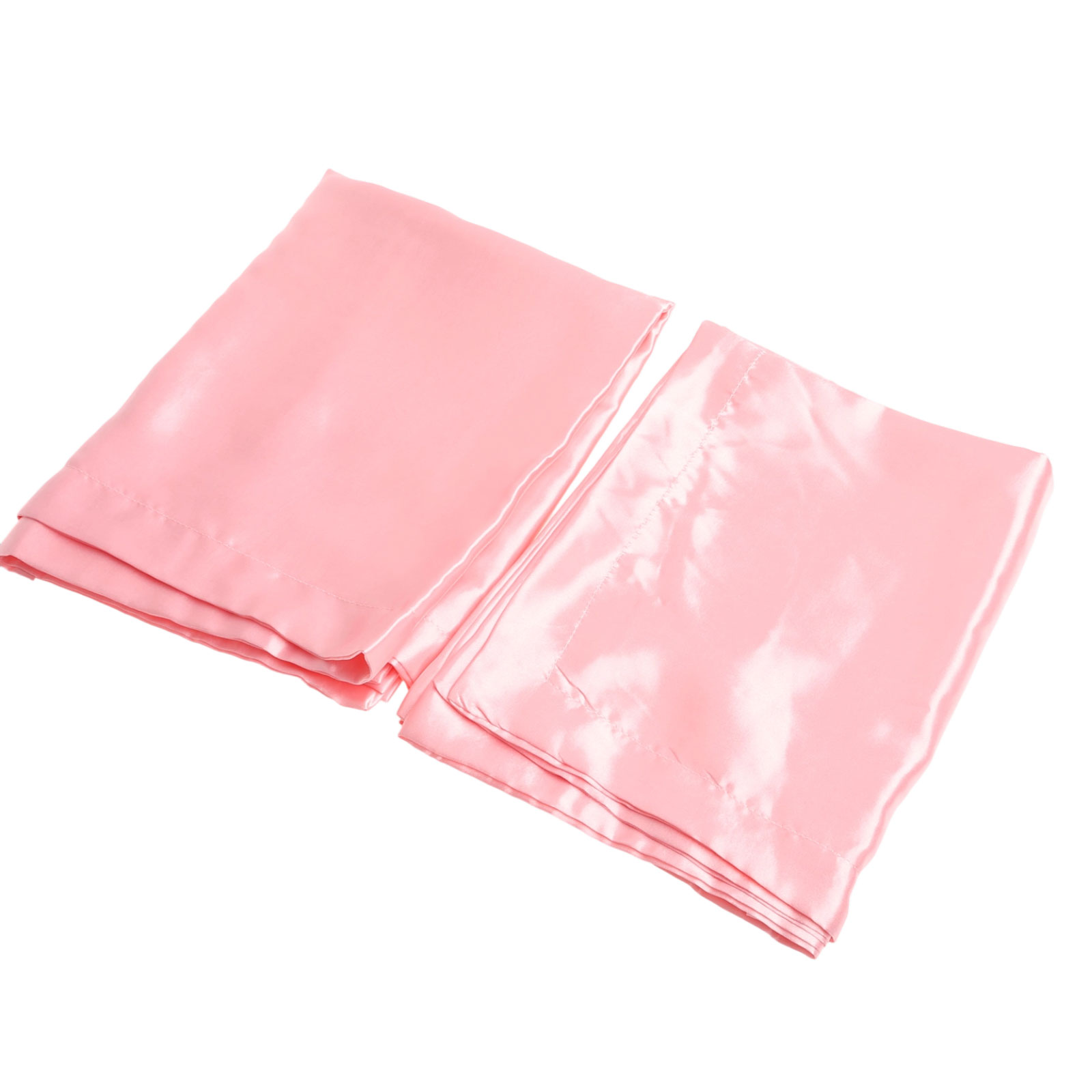 Zwei rosa Satin-Kissenbezüge auf weißem Hintergrund. Der Stoff reflektiert das Licht und zeigt Falten und Nähte.