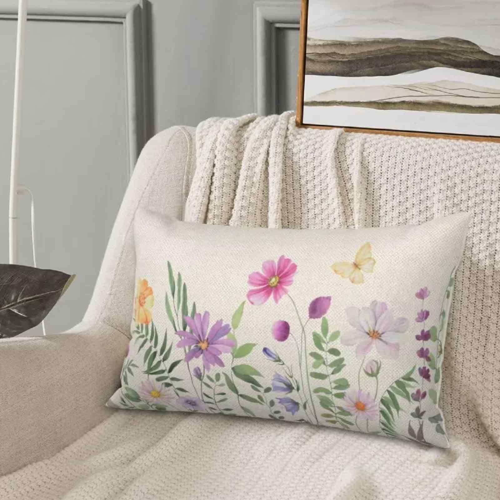 Kissen mit Blumendesign auf einem Stuhl mit einer Decke. Schmetterlinge und Blumen in Rosa, Lila und Gelb sind sichtbar.