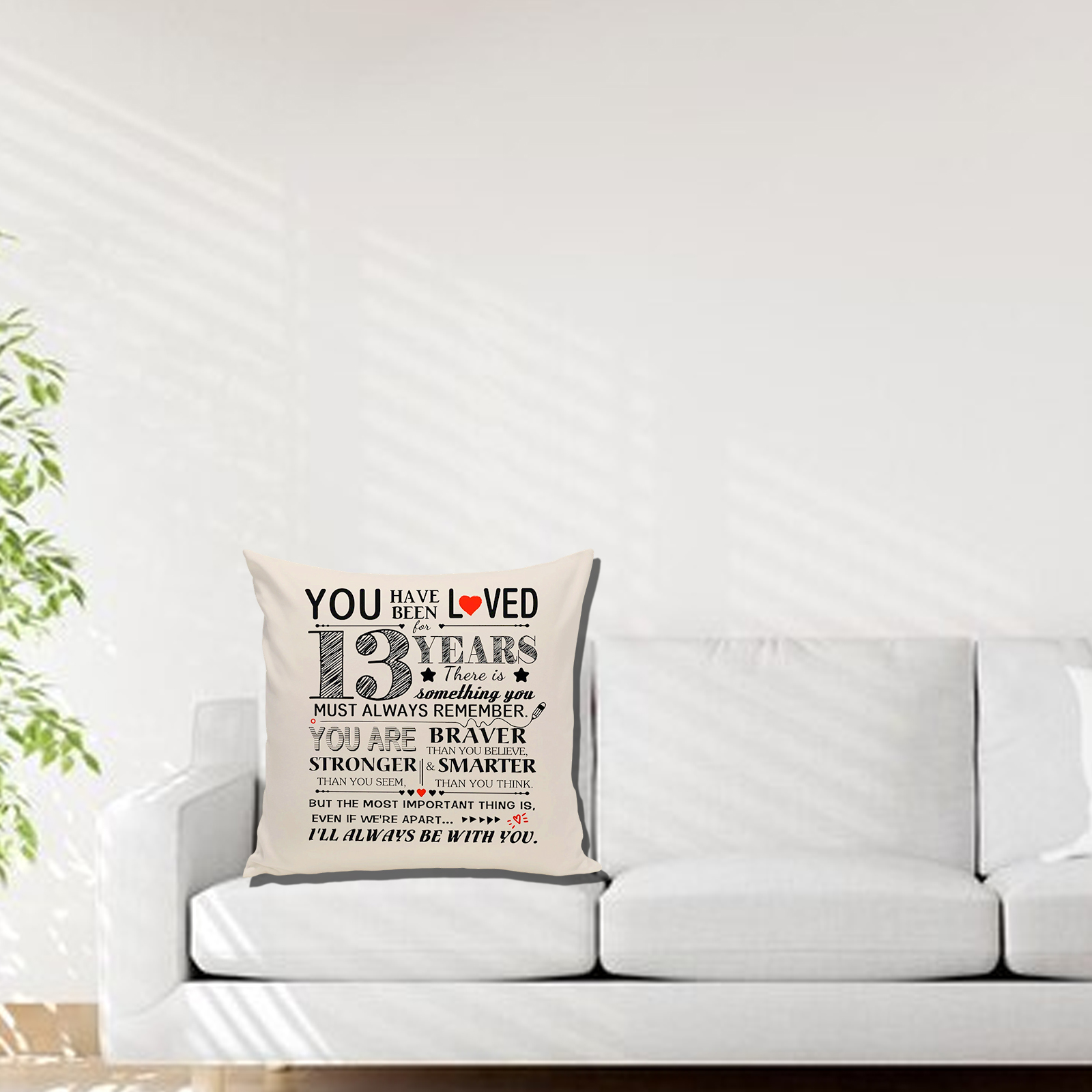 Ein weißes Kissen auf einem weißen Sofa. Es hat Text mit der Aufschrift 'Du wurdest 13 Jahre lang geliebt'. Der Hintergrund ist eine weiße Wand.