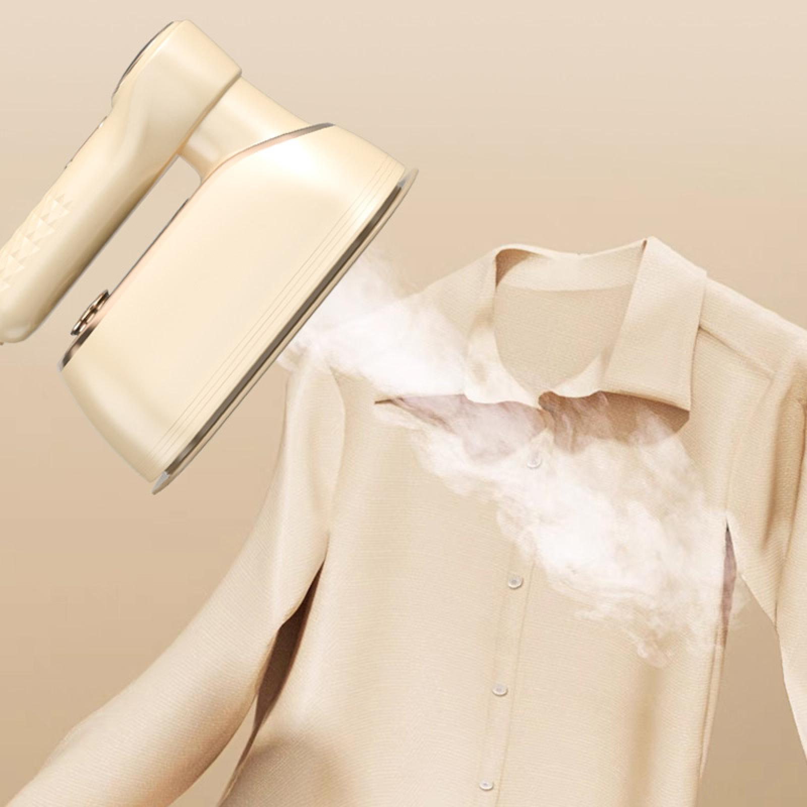 Ein cremefarbener Kleidungsdampfer dampft ein hellbeige Hemd. Dampf quillt aus dem Dampfer auf das Hemd.