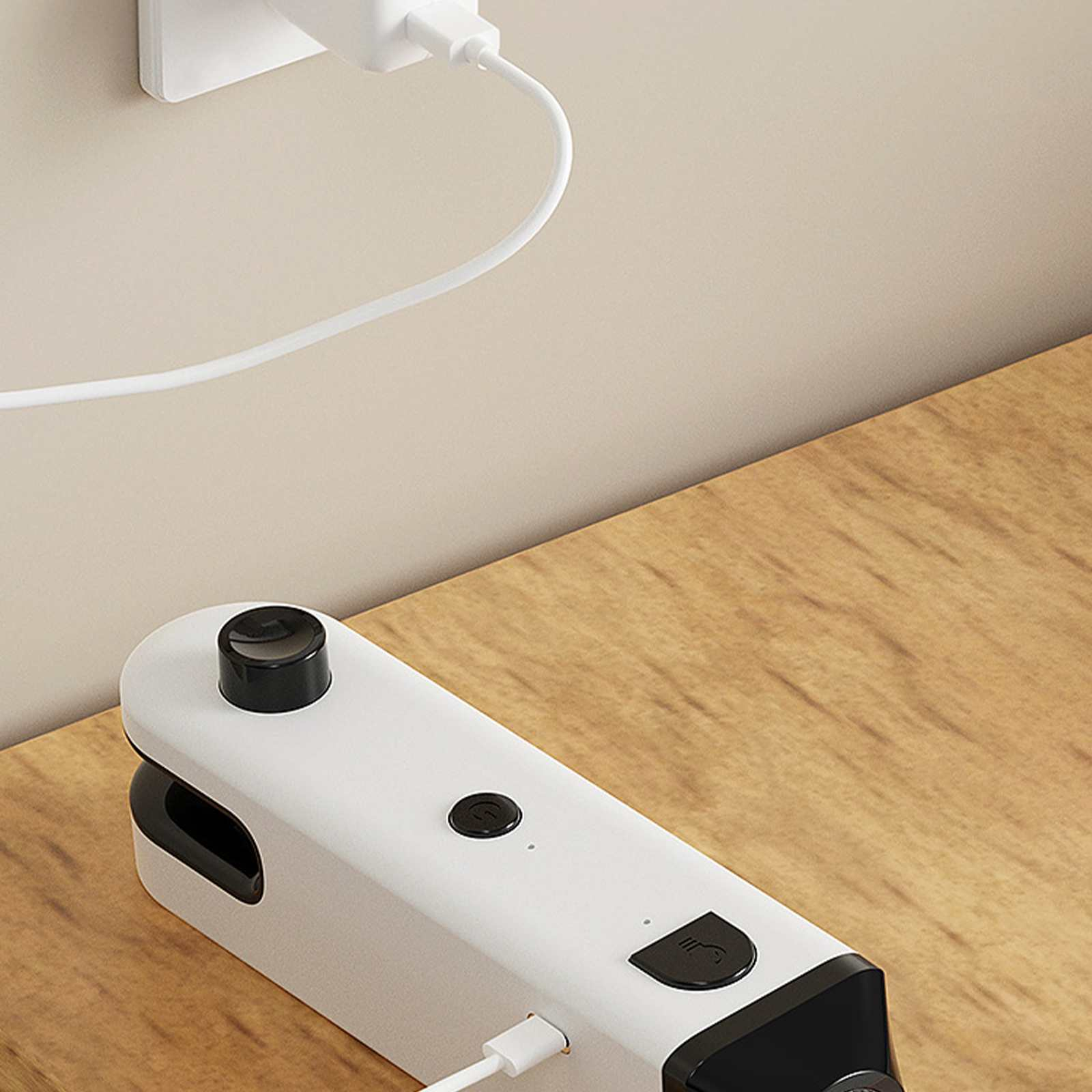Ein weißes und schwarzes Gerät mit Ladekabel liegt auf einer Holzoberfläche. Ein weißes Ladegerät ist an der Wand.