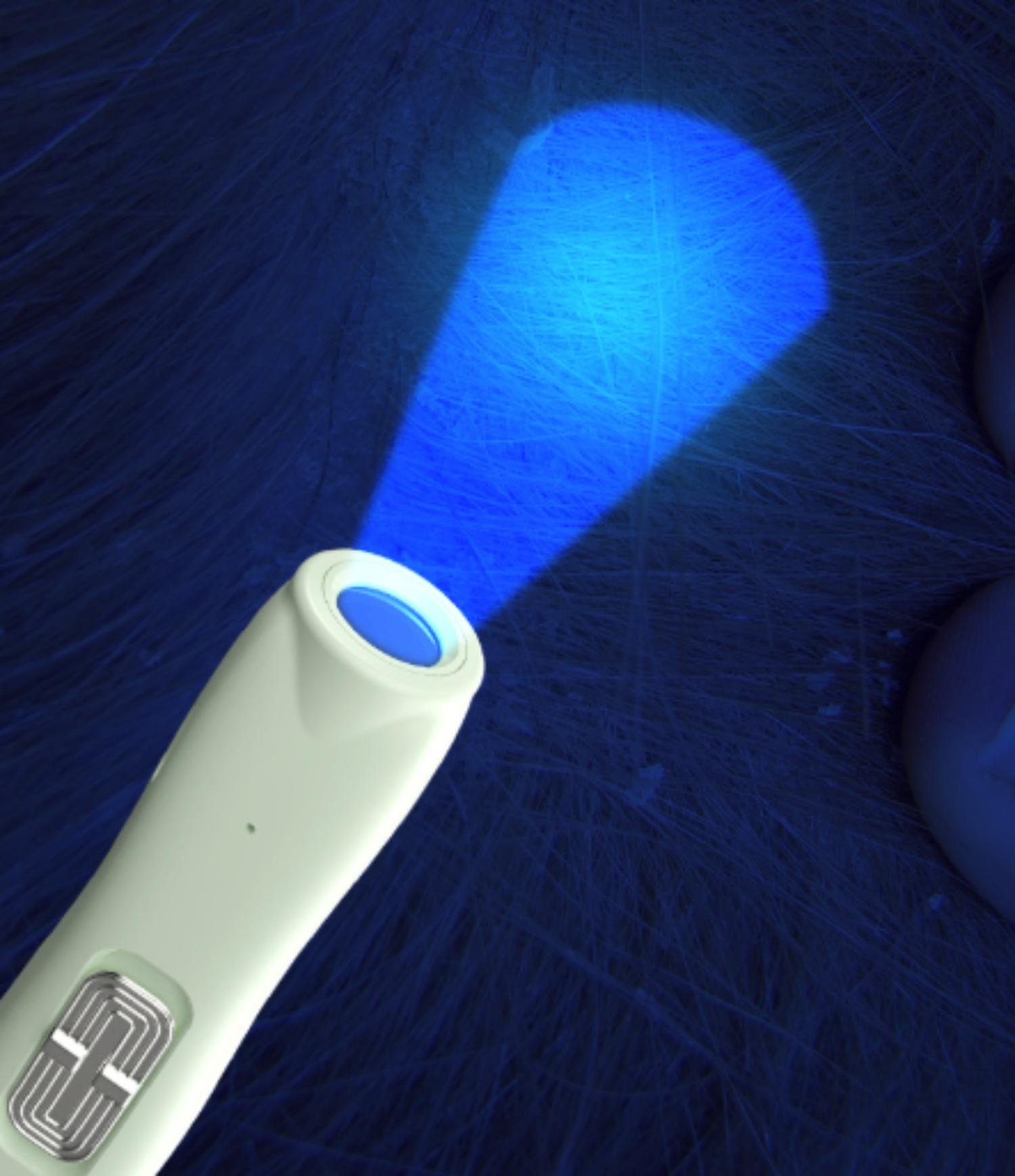Ein blaues Licht scheint von einem Handgerät auf eine dunkle Oberfläche. Licht zeigt Fasern. Das Gerät ist weiß-grün.