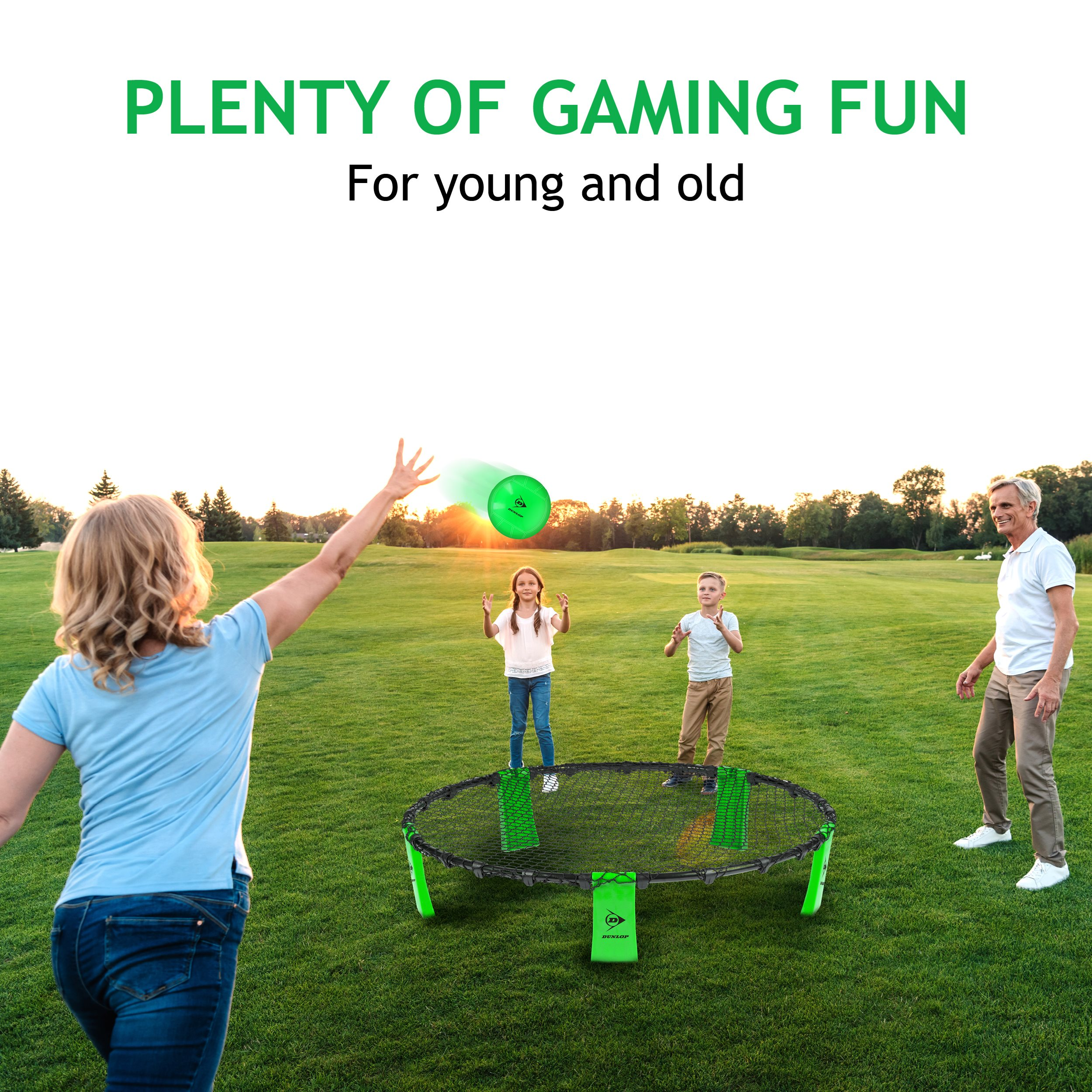 Een gezin speelt spikeball op een groen gazon. Een groene bal is in beweging. Bomen staan op de achtergrond.