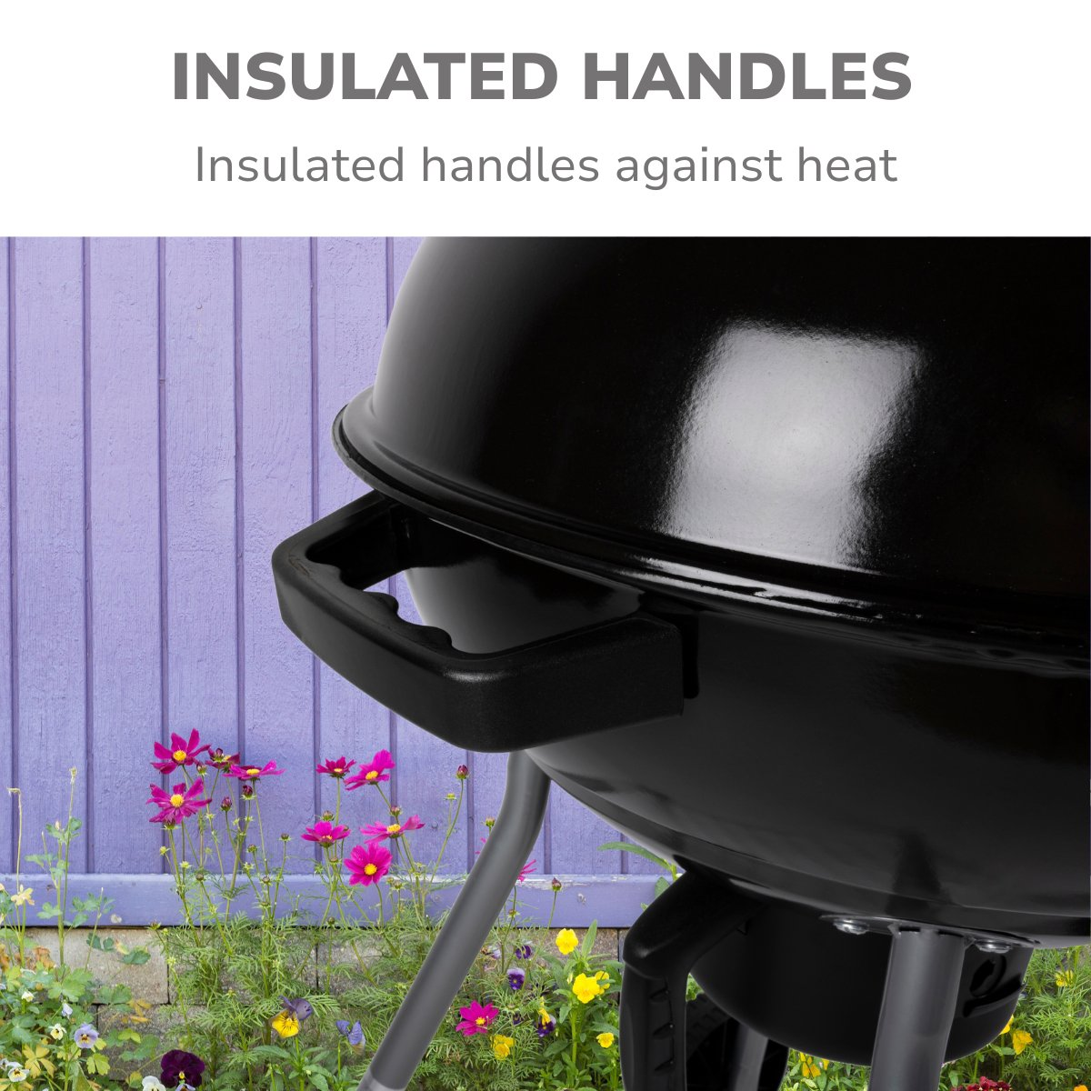 Zwarte grill met geïsoleerde handvatten, bloemen voor een paarse houten hek. De grill staat in de tuin.
