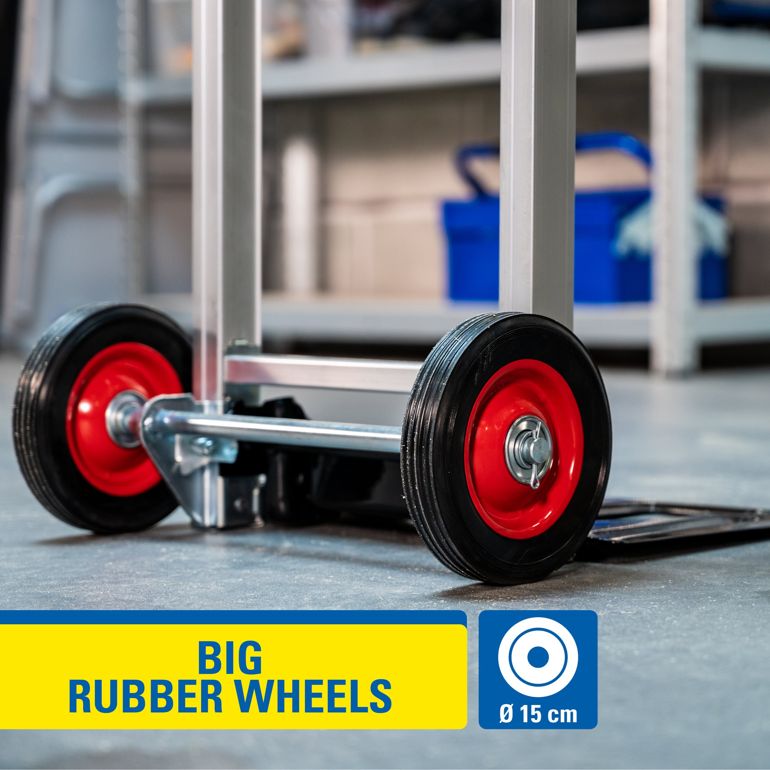 Hand truck with large rubber wheels. Black tires with red rims. A yellow and blue sign says BIG RUBBER WHEELS.