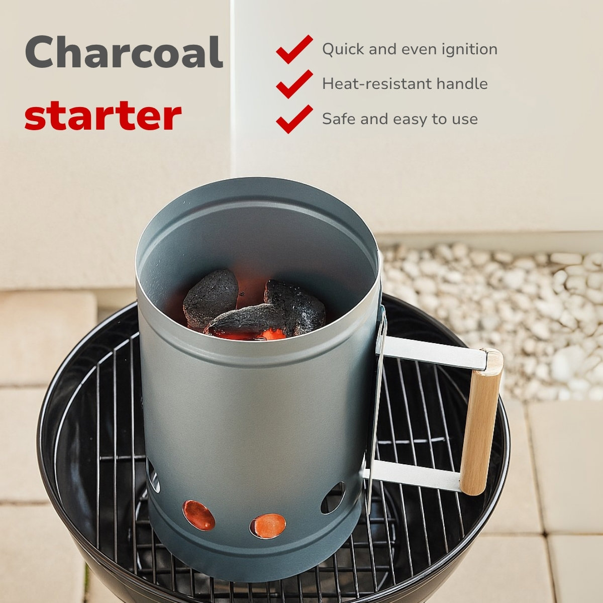 A charcoal starter on a grill. The starter is cylindrical, grey, with burning charcoal inside. Features include a wooden handle.