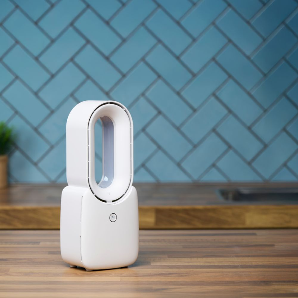 Purificateur d'air blanc sur surface en bois, fond de mur carrelé bleu. Petite plante à gauche. Le purificateur est le sujet principal.