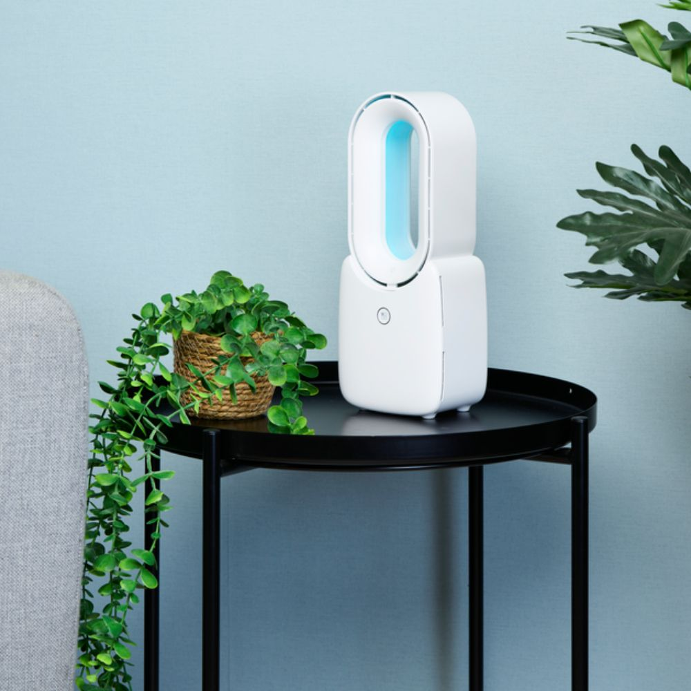 Un purificateur d'air blanc avec une lumière bleue est sur une table noire. Une plante en pot à côté. Fond bleu.