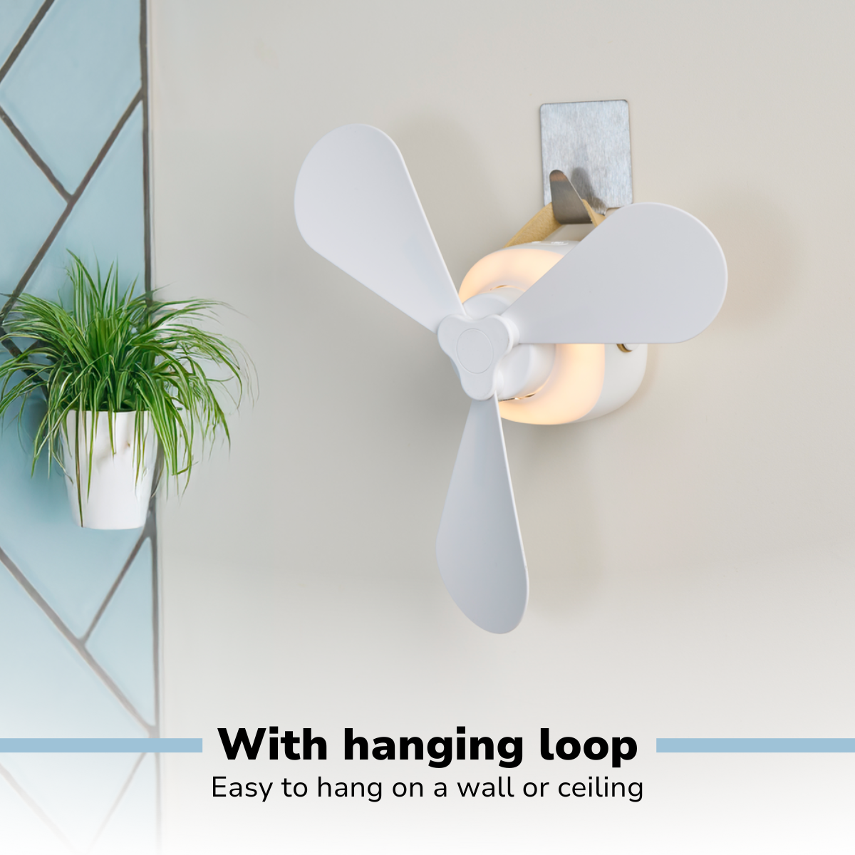 Un ventilateur blanc à trois pales est monté sur un mur. Une plante dans un pot blanc est suspendue à gauche. Le ventilateur a une boucle de suspension.