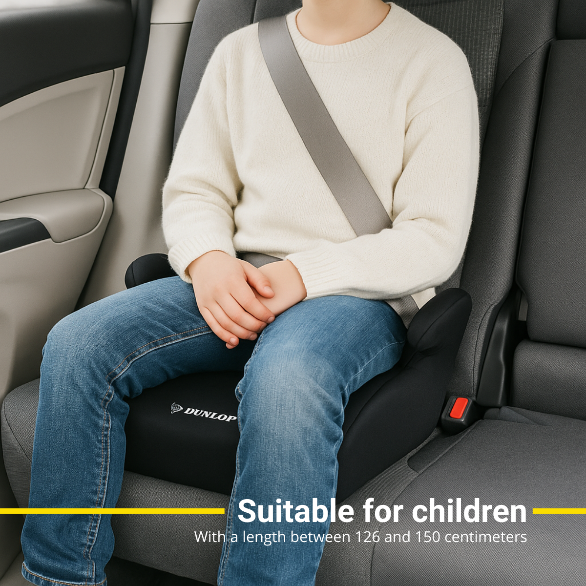 Een kind met een veiligheidsgordel zit in een autostoel. De stoel is zwart en zegt Dunlop. Het interieur van de auto is grijs.