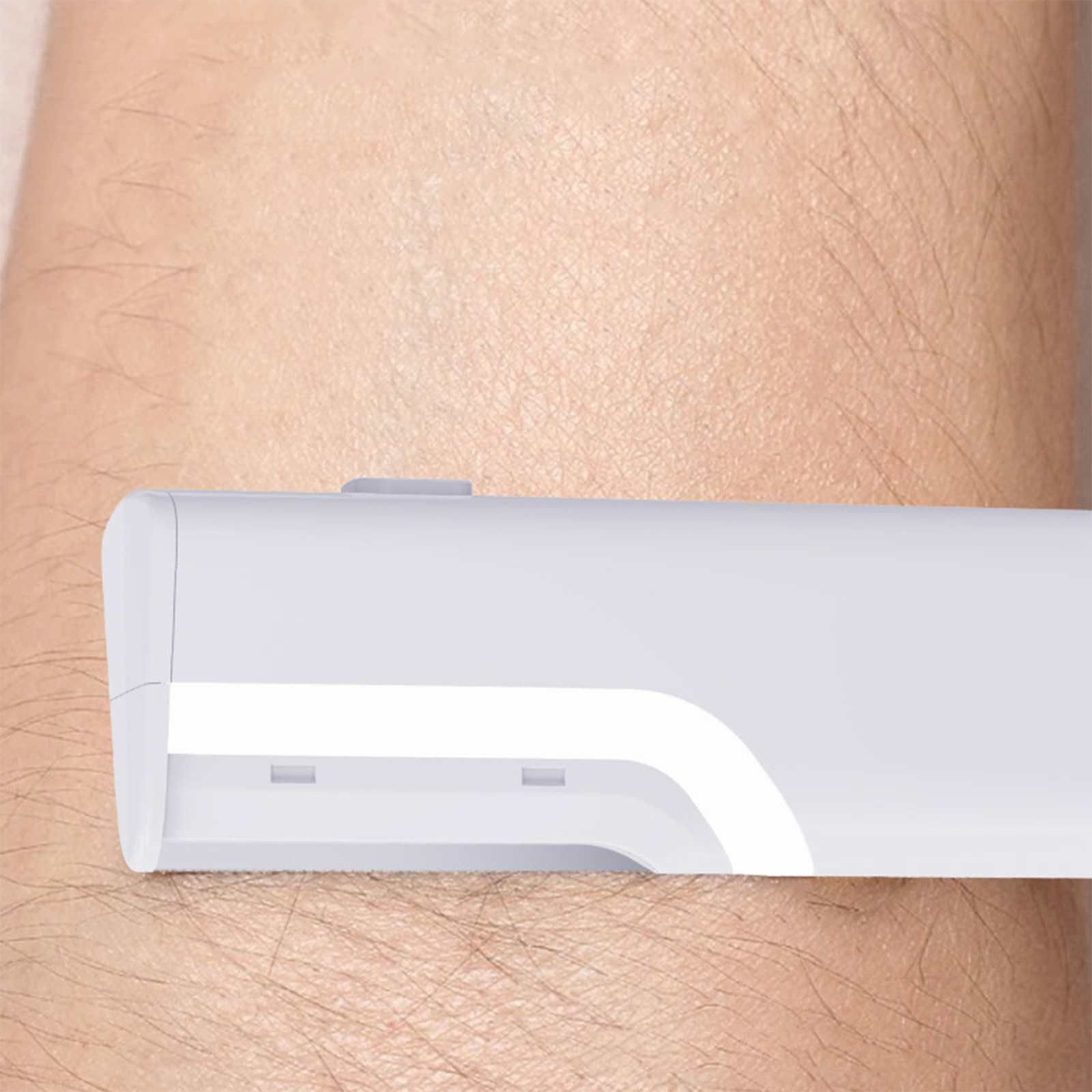 Ein weißes Gerät liegt auf einem behaarten Arm. Das Gerät hat einen Lichtstreifen. Der Arm ist hellbraun.