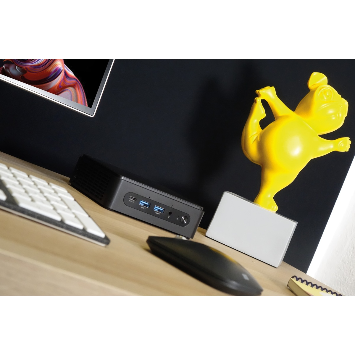 Konfiguracja pulpitu z komputerem, klawiaturą, myszą i żółtą statuetką psa uprawiającego jogę na biurku.