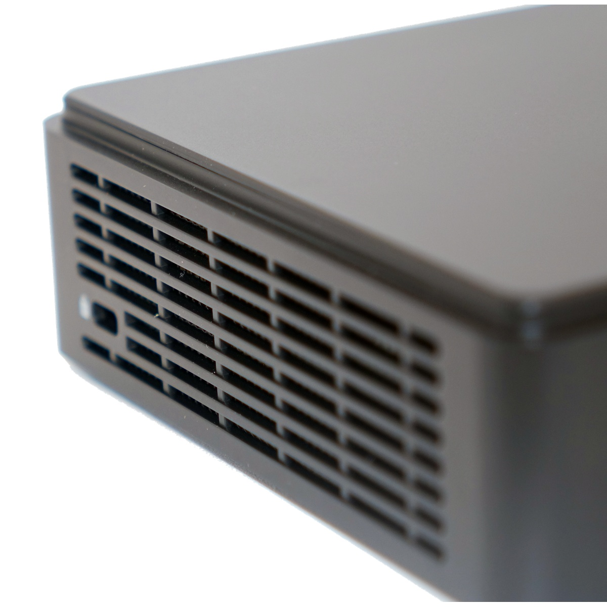 Zbliżenie ciemnoszarego urządzenia elektronicznego. Z boku widać otwór wentylacyjny z równoległymi szczelinami. Góra jest gładka, a tło białe.