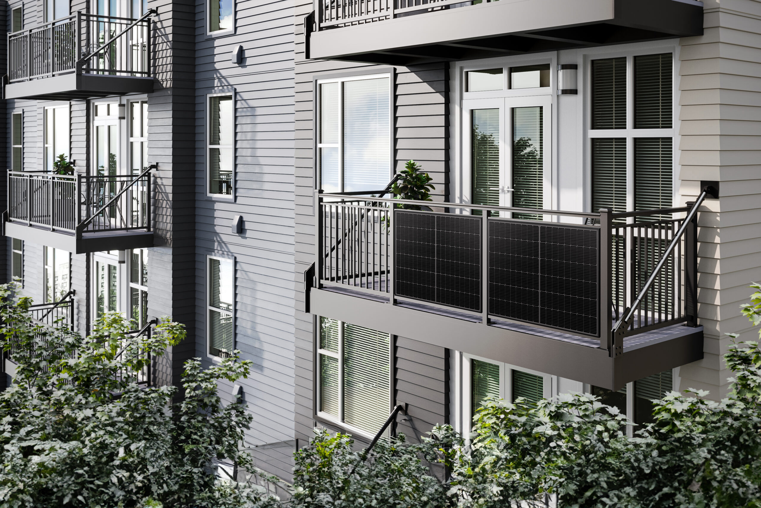 Edificio de apartamentos con balcones. Revestimiento gris, barandillas negras, árboles en primer plano. El balcón tiene paneles negros.