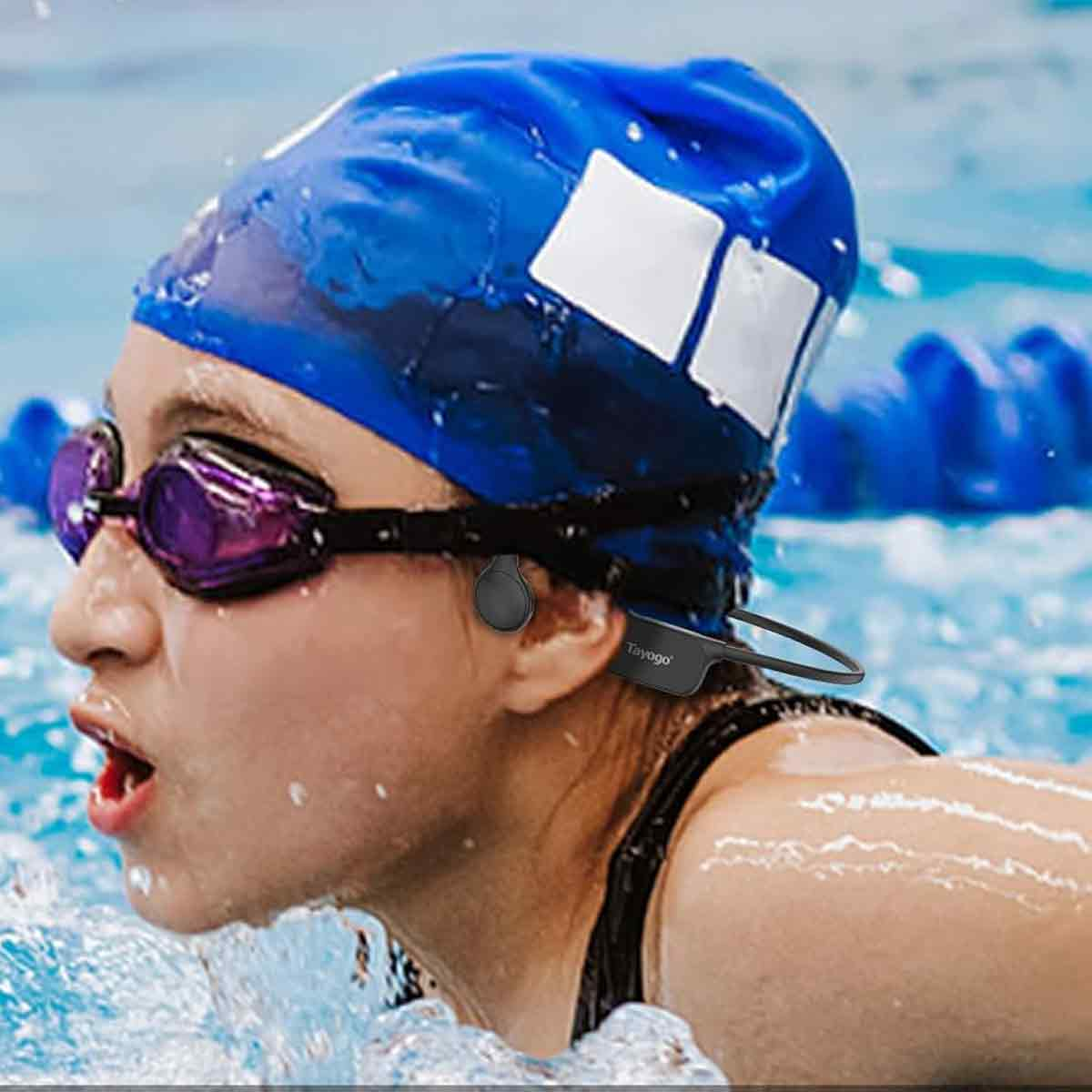 Eine Schwimmerin mit Brille und Mütze schwimmt im Pool. Sie trägt wasserdichte Kopfhörer. Der Hintergrund zeigt das Schwimmbecken.