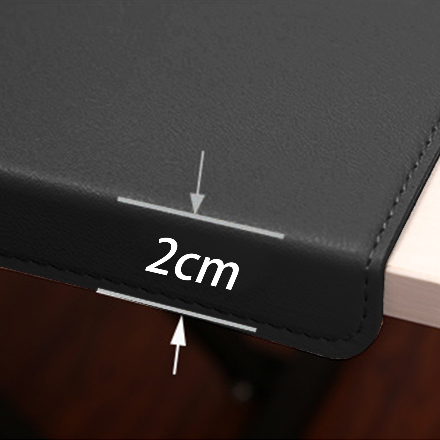 Zbliżenie czarnego skórzanego przedmiotu z białą etykietą '2cm', mierzone strzałkami. Obiekt leży na drewnianej powierzchni.