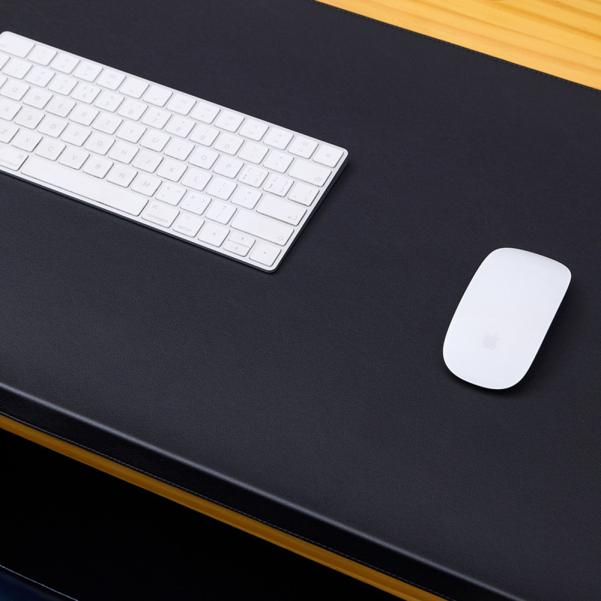 Biała klawiatura i mysz na czarnym biurku. Biurko ma drewnianą ramę. Tło jest rozmyte.