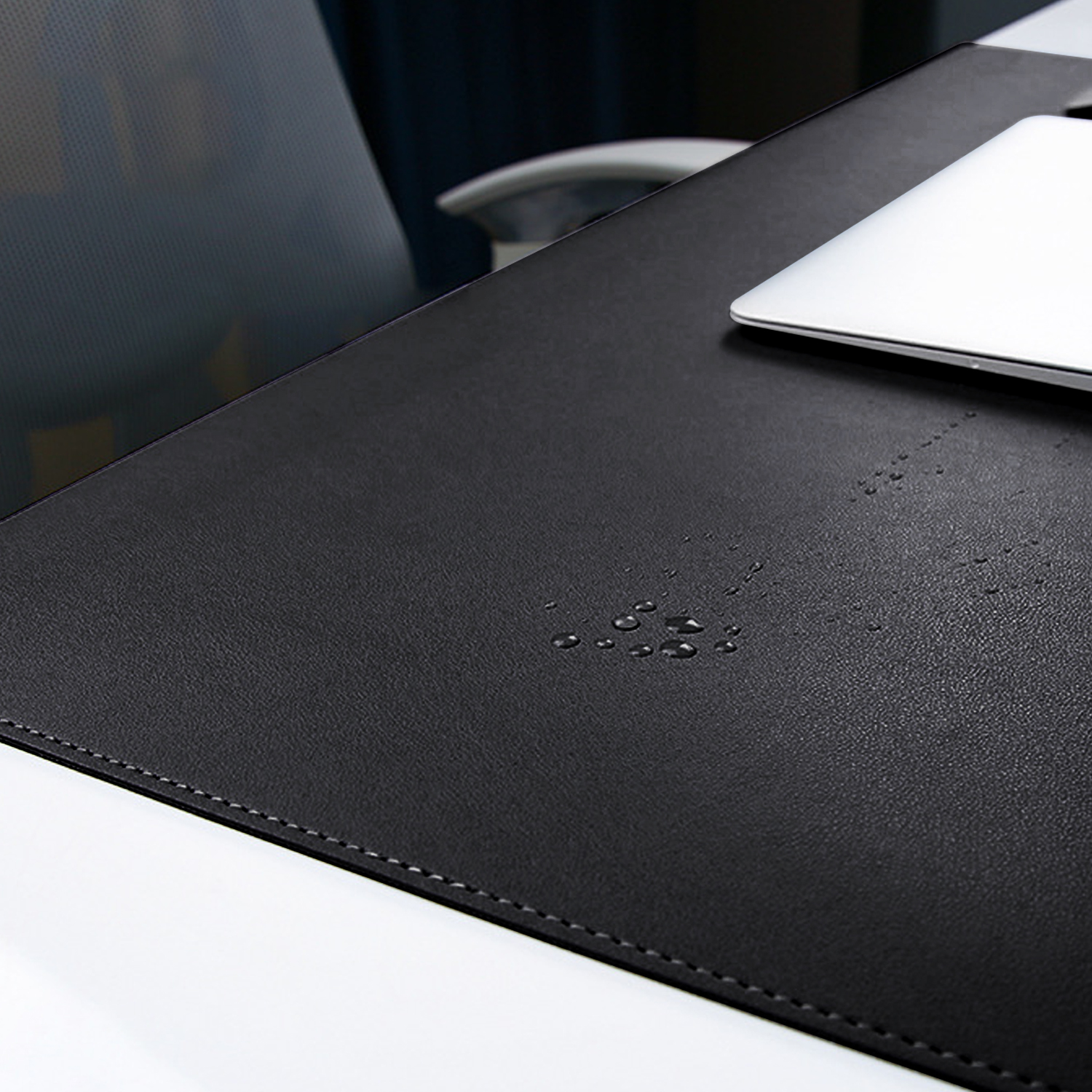 Czarna podkładka na biurko z kroplami wody i laptopem, biały stół i szare krzesło biurowe są widoczne na scenie.