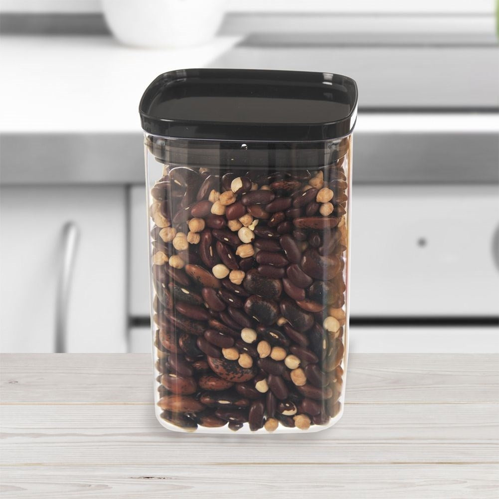 Un recipiente transparente lleno de frijoles. El recipiente tiene una tapa negra. El fondo muestra una encimera de cocina.