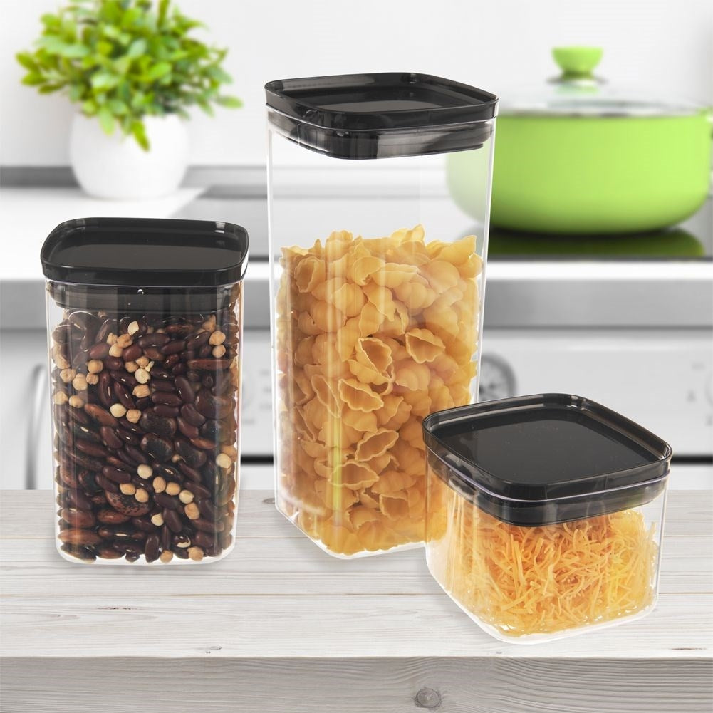 Tres recipientes transparentes con tapas negras. Uno tiene frijoles, otro conchas de pasta y el último queso rallado. Fondo de cocina.