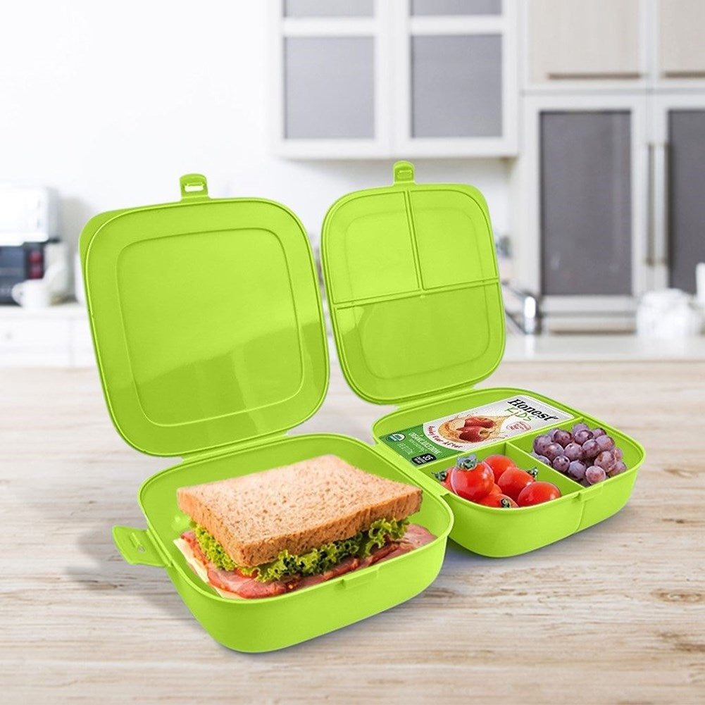 Tres fiambreras verdes abiertas sobre una superficie de madera. Una contiene un sándwich, las otras tomates, uvas y comida envasada.