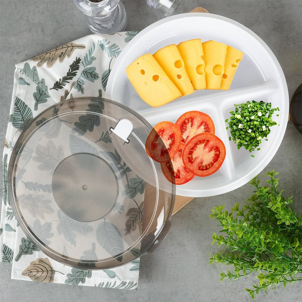 Un plato blanco dividido contiene rebanadas de queso, rebanadas de tomate y verduras picadas. Una tapa transparente está al lado.
