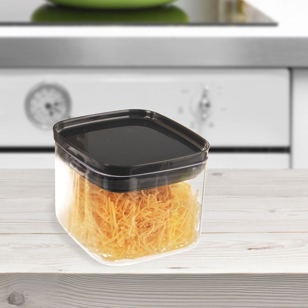 Un recipiente transparente con tapa negra lleno de comida naranja rallada, sobre una superficie de madera. Se ve un fondo de cocina.