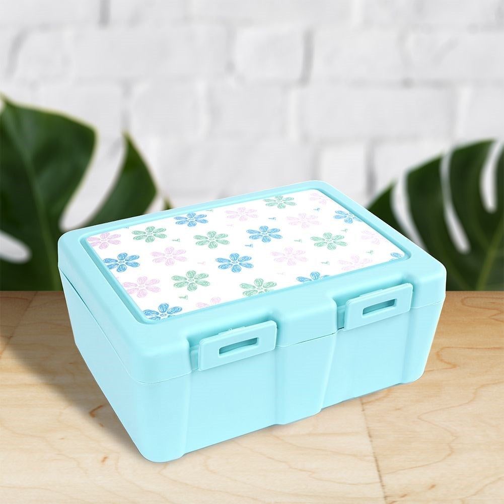 Una fiambrera azul claro con una tapa estampada floral. El fondo presenta una pared de ladrillos y hojas verdes.