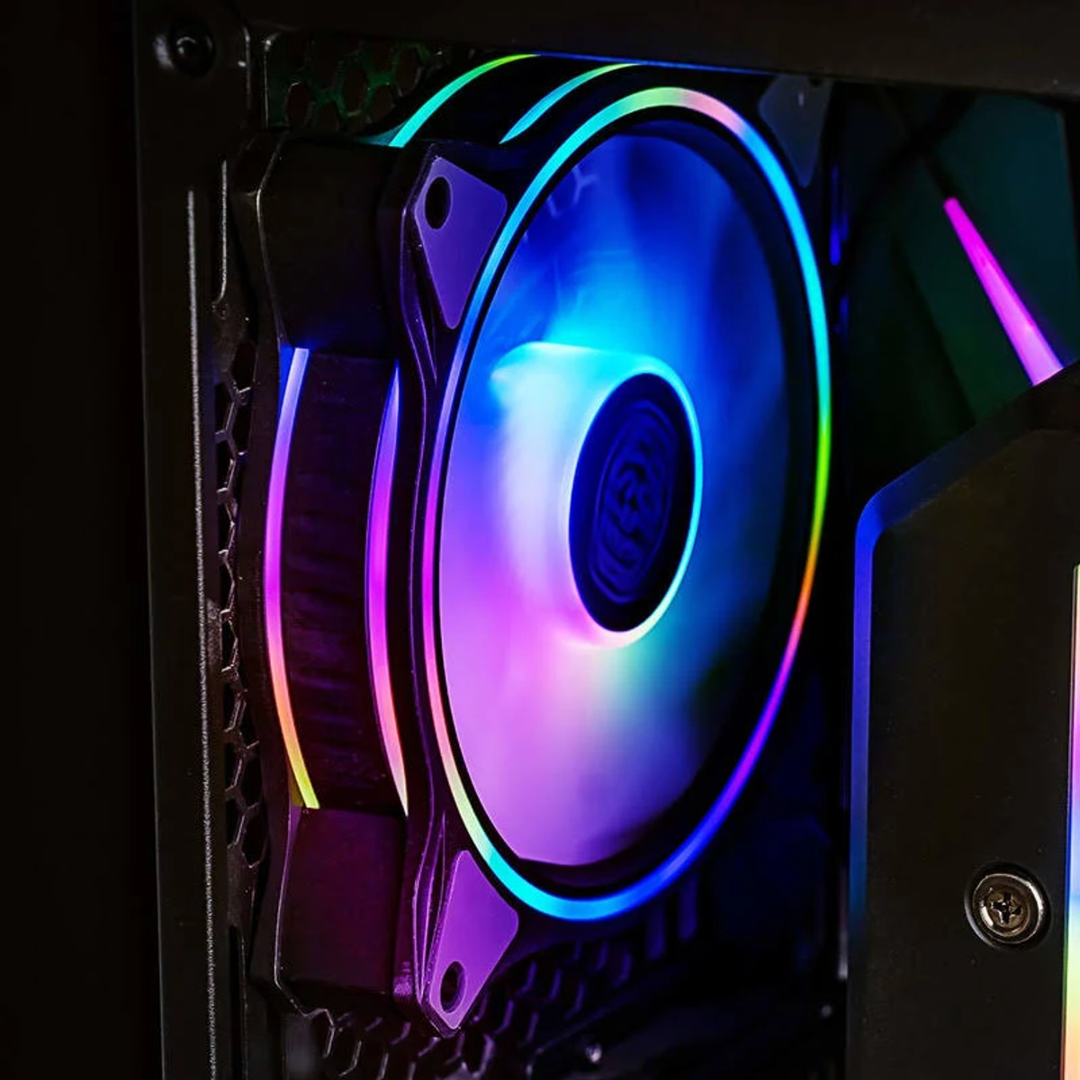 Primo piano di una ventola per computer con illuminazione RGB colorata. La ventola è all'interno di un case scuro.