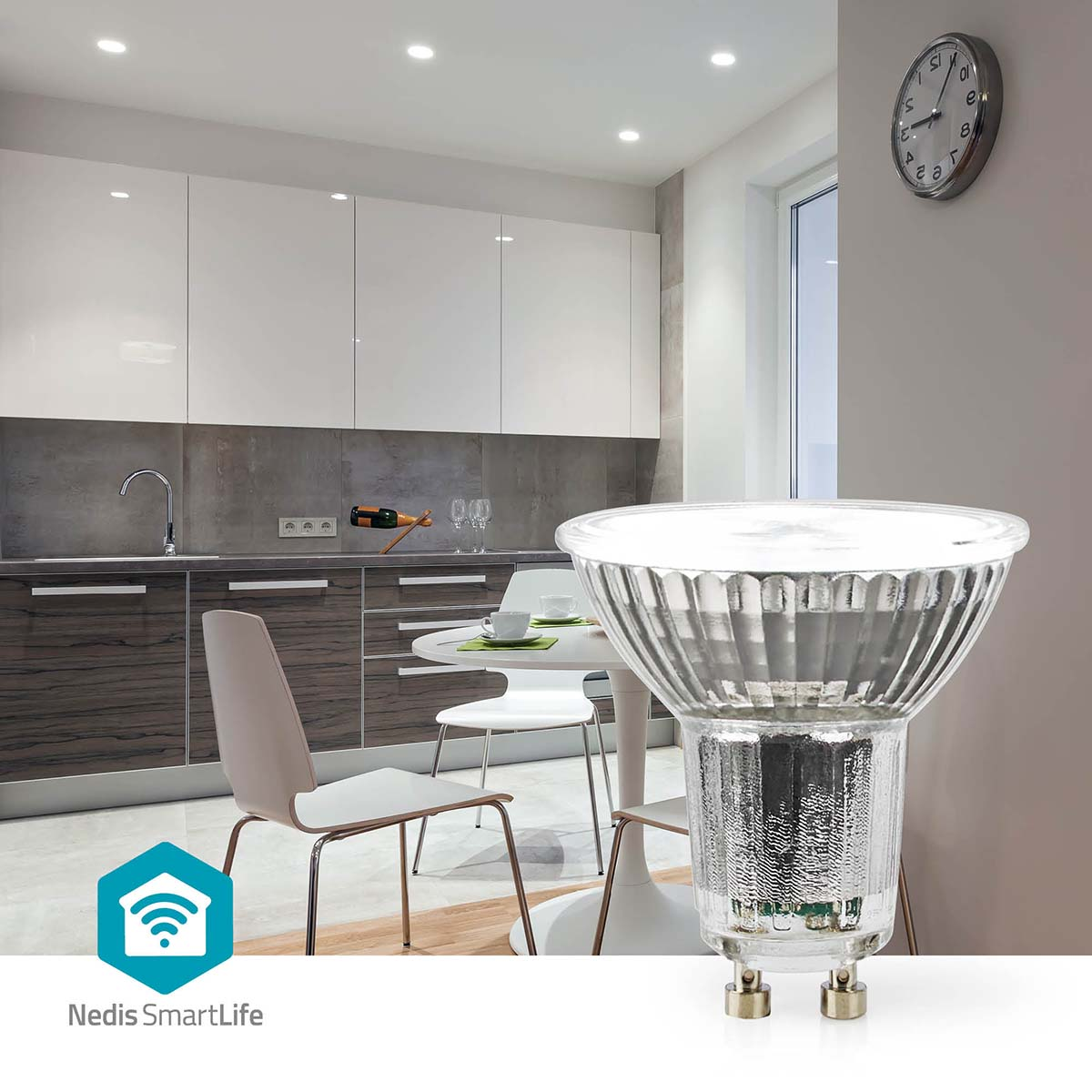 Scena kuchenna z żarówką na pierwszym planie. W tle widoczne są szafki, stół, krzesła i zegar.