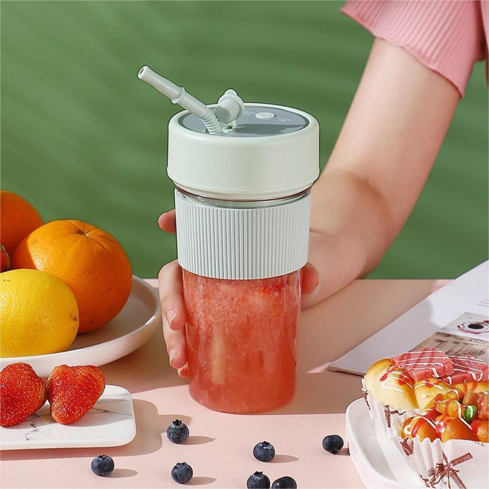 Eine Hand hält einen Mixer mit einem rosa Smoothie. Orangen, Erdbeeren, Blaubeeren und Gebäck sind in der Nähe.