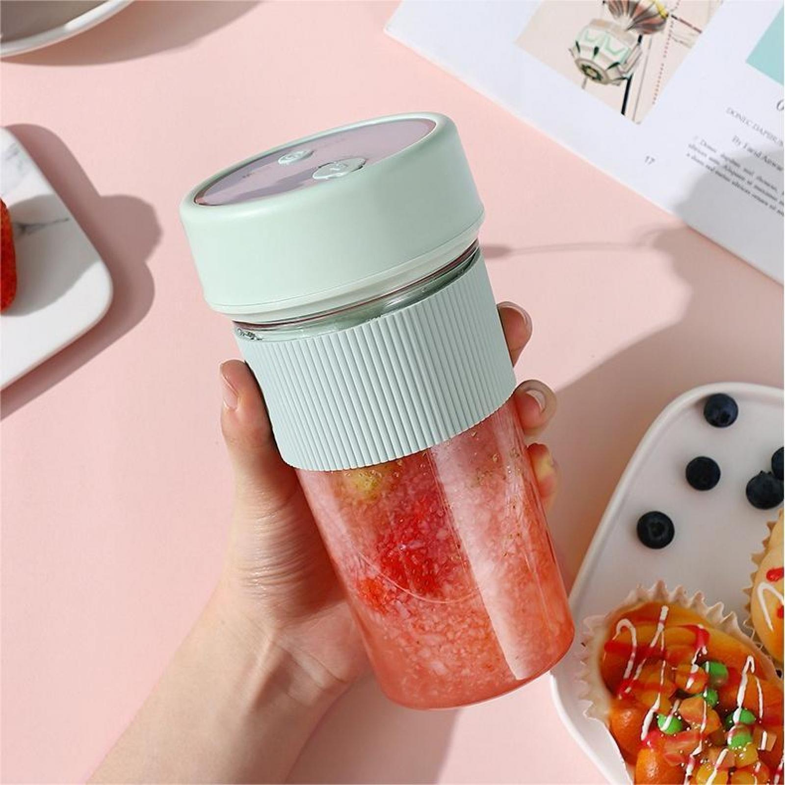 Eine Hand hält einen grünen Mixer mit rotem Smoothie. Daneben ist ein Teller mit Gebäck und Blaubeeren zu sehen.