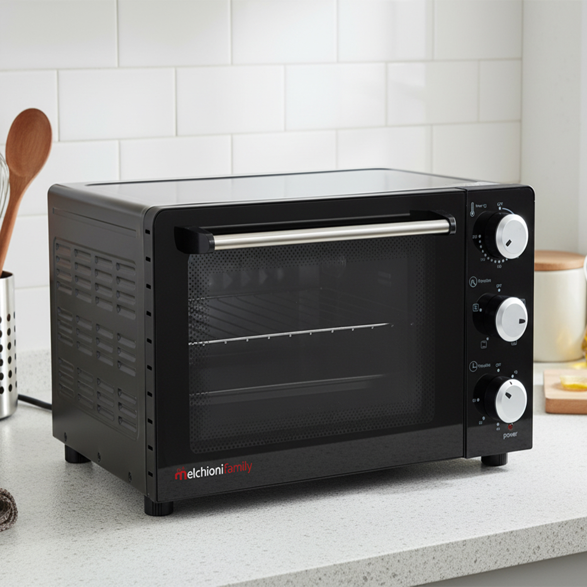 Czarny piekarnik na blacie stoi na białym blacie. Ma szklane drzwi i pokrętła. Po lewej stronie drewniana łyżka i trzepaczka.