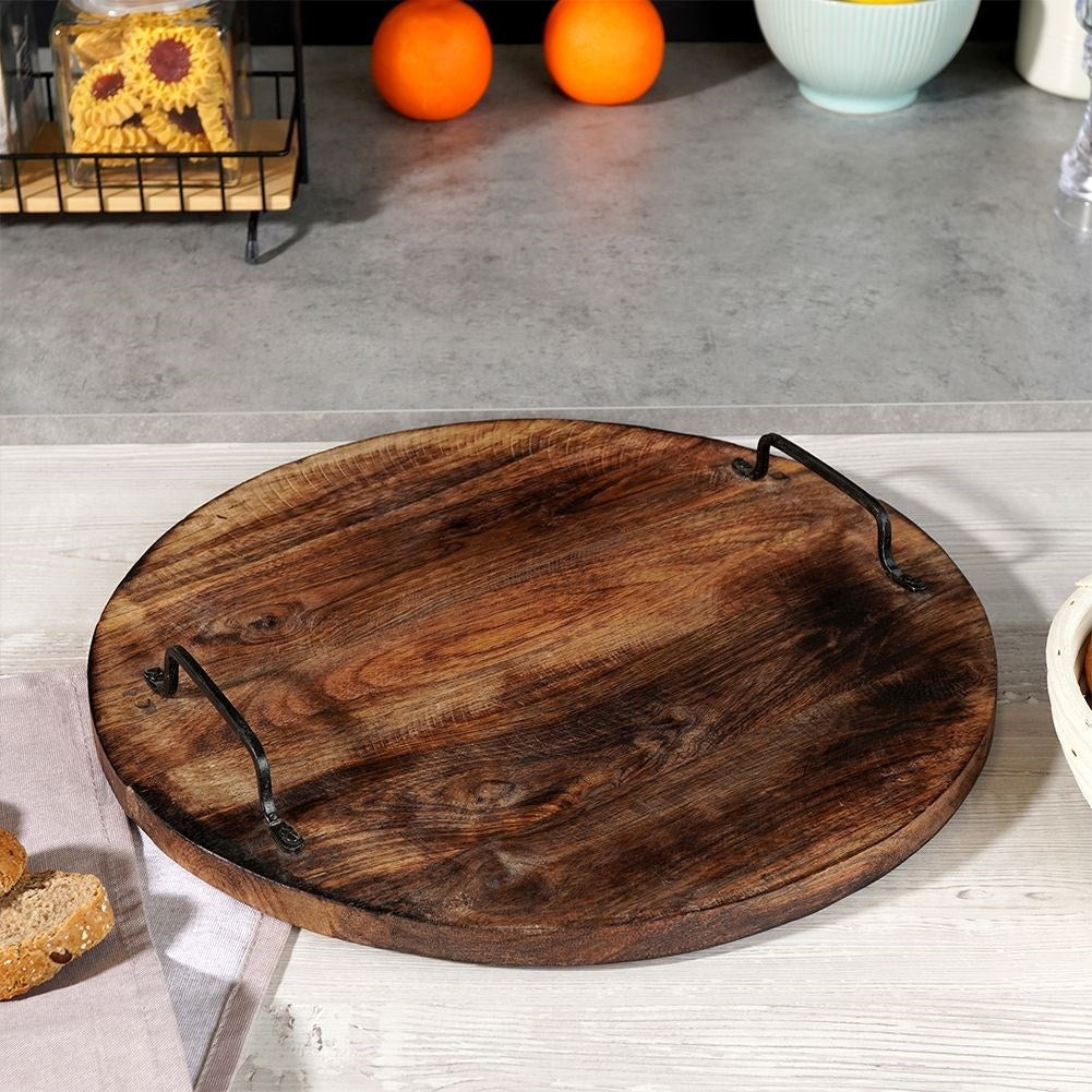 Una bandeja redonda de madera con asas. Naranjas y galletas en el fondo. Pan y una servilleta en primer plano.