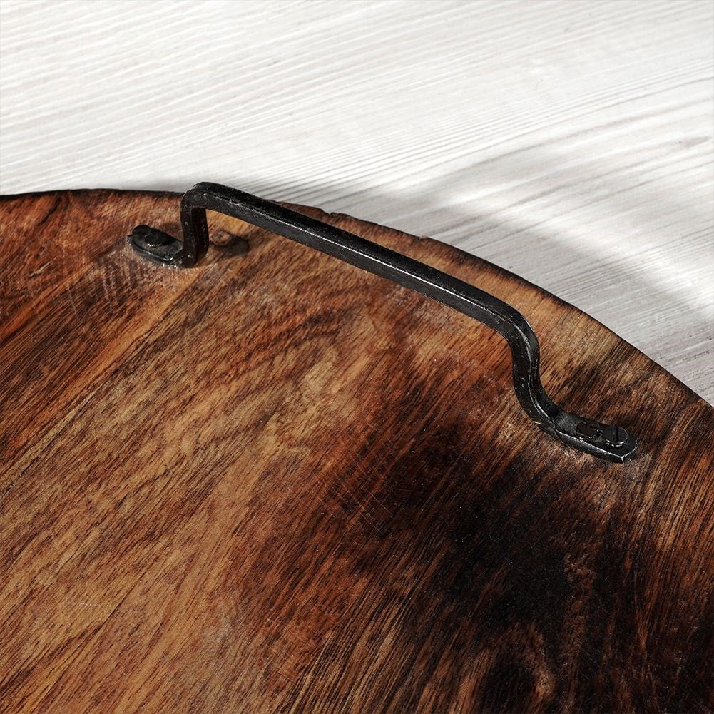 Primer plano de una bandeja de madera con asa de metal negro. La bandeja tiene vetas oscuras. El fondo es de madera blanca.