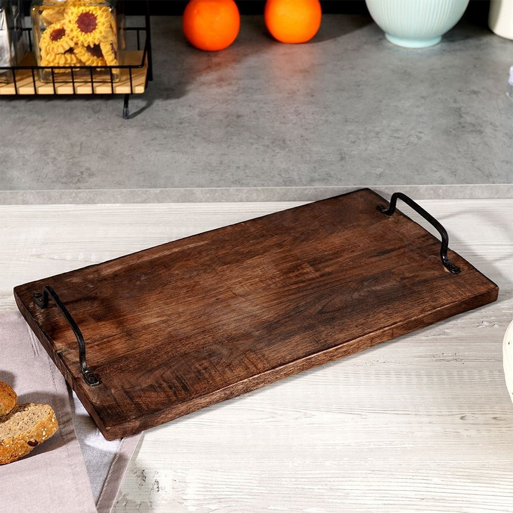 Un vassoio di legno con manici neri su un tavolo di legno chiaro. Arance, biscotti e pane sullo sfondo.