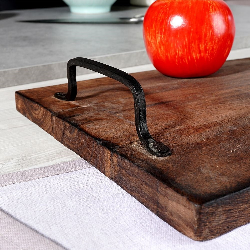 Vassoio in legno con manico nero, mela rossa e panno bianco in primo piano. Altri oggetti sullo sfondo.
